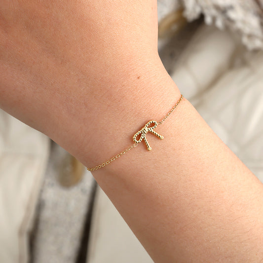 Gold beaded bow bracelet on delicate chain embodying quiet feminine grace