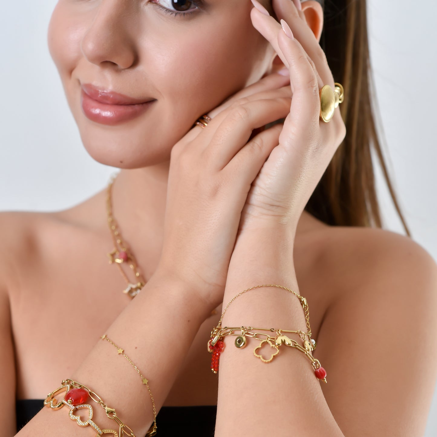 Woman wearing gold jewelry including a necklace, bracelet, and ring on a plain background