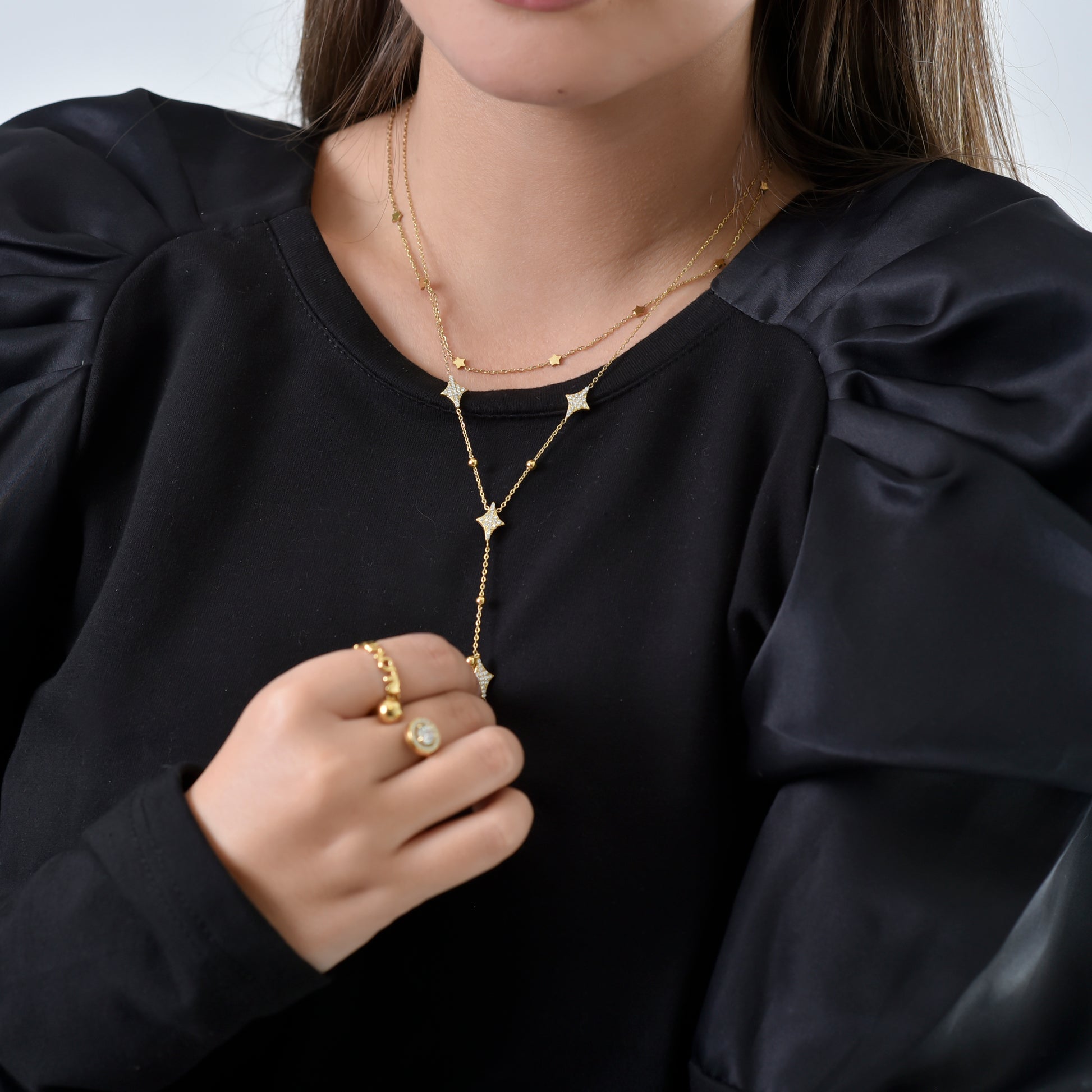 Person wearing a gold necklace and ring on a plain background