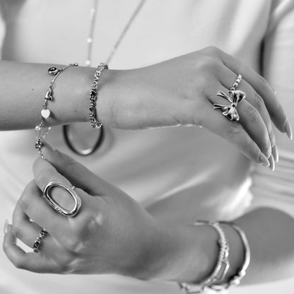 Close-up of hands wearing multiple silver rings and bracelets on a neutral background