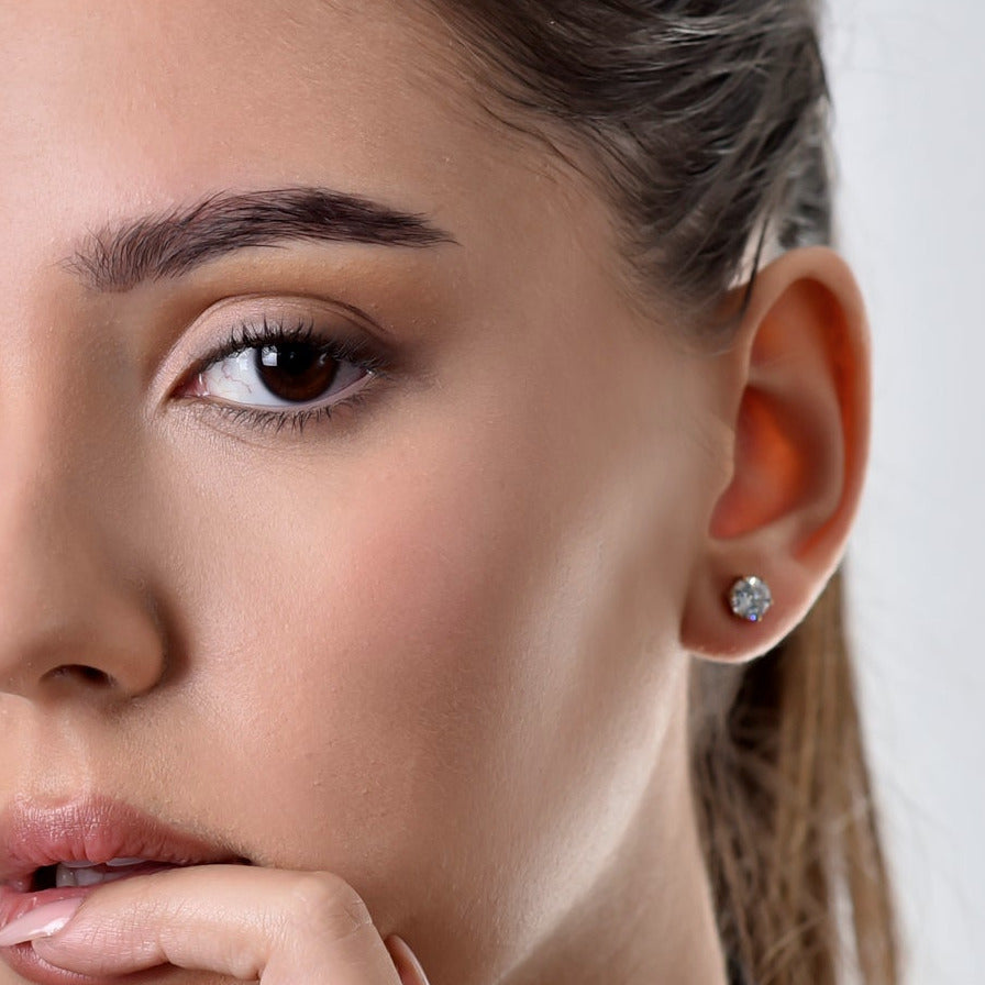 Woman wearing gold jewelry including a ring, bracelet, and earrings on a plain background