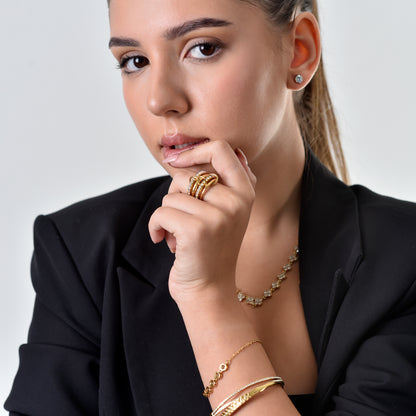Woman wearing gold jewelry including a ring, bracelet, and necklace on a plain background