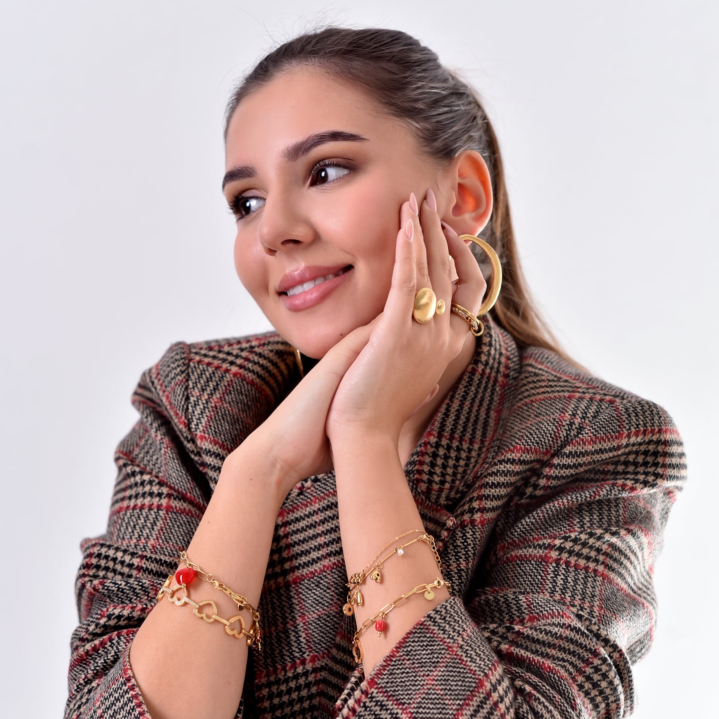 Woman wearing gold jewelry including earrings, rings, and bracelets on a white background