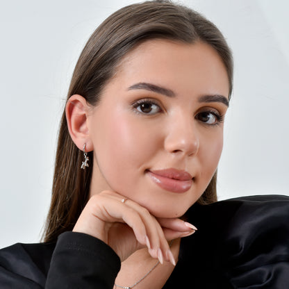 Woman with long brown hair wearing earrings and a black top against a white background