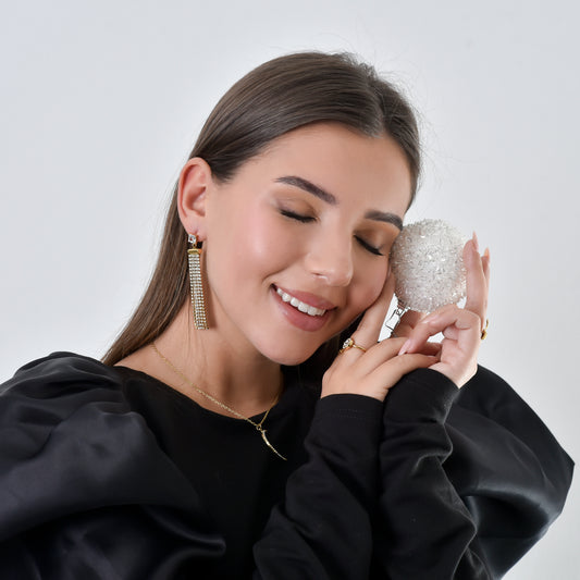 Woman wearing sparkling earrings and holding a decorative item against a plain background