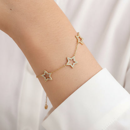 Gold star bracelet on a person's wrist with a neutral background
