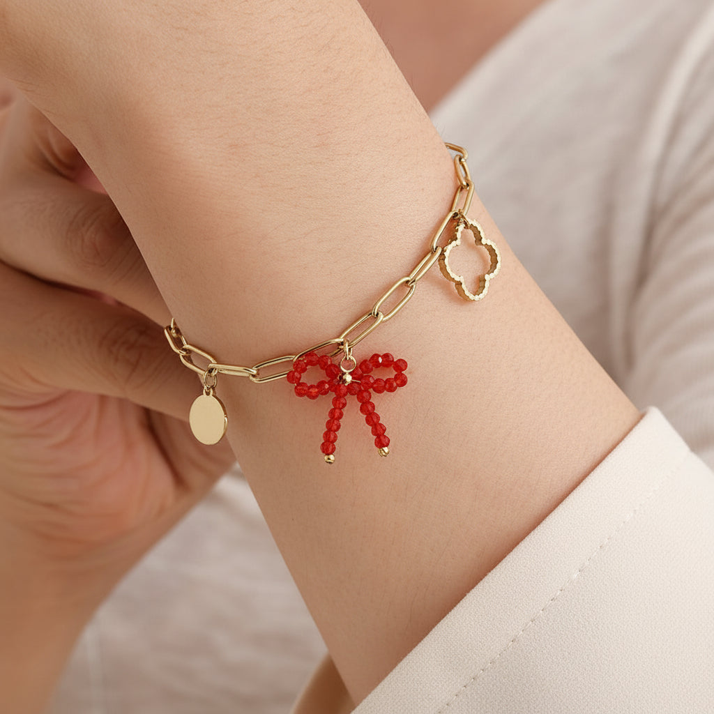 Gold paperclip chain bracelet with mixed charms including crystal beaded bow, freshwater pearl, clover, and disc